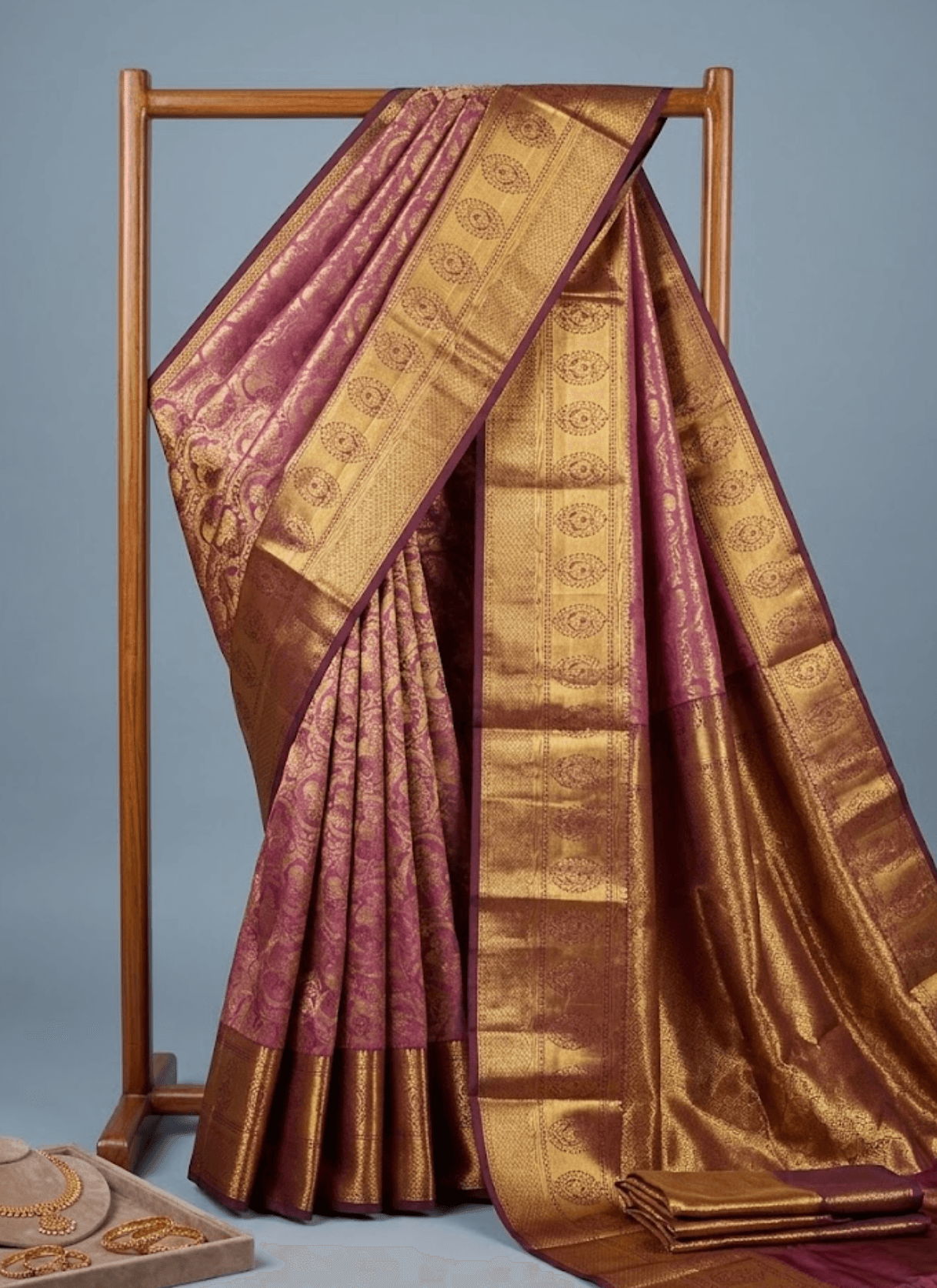 A stunning pink saree adorned with intricate golden zari motifs, beautifully paired with a rich coffee-brown contrast border.